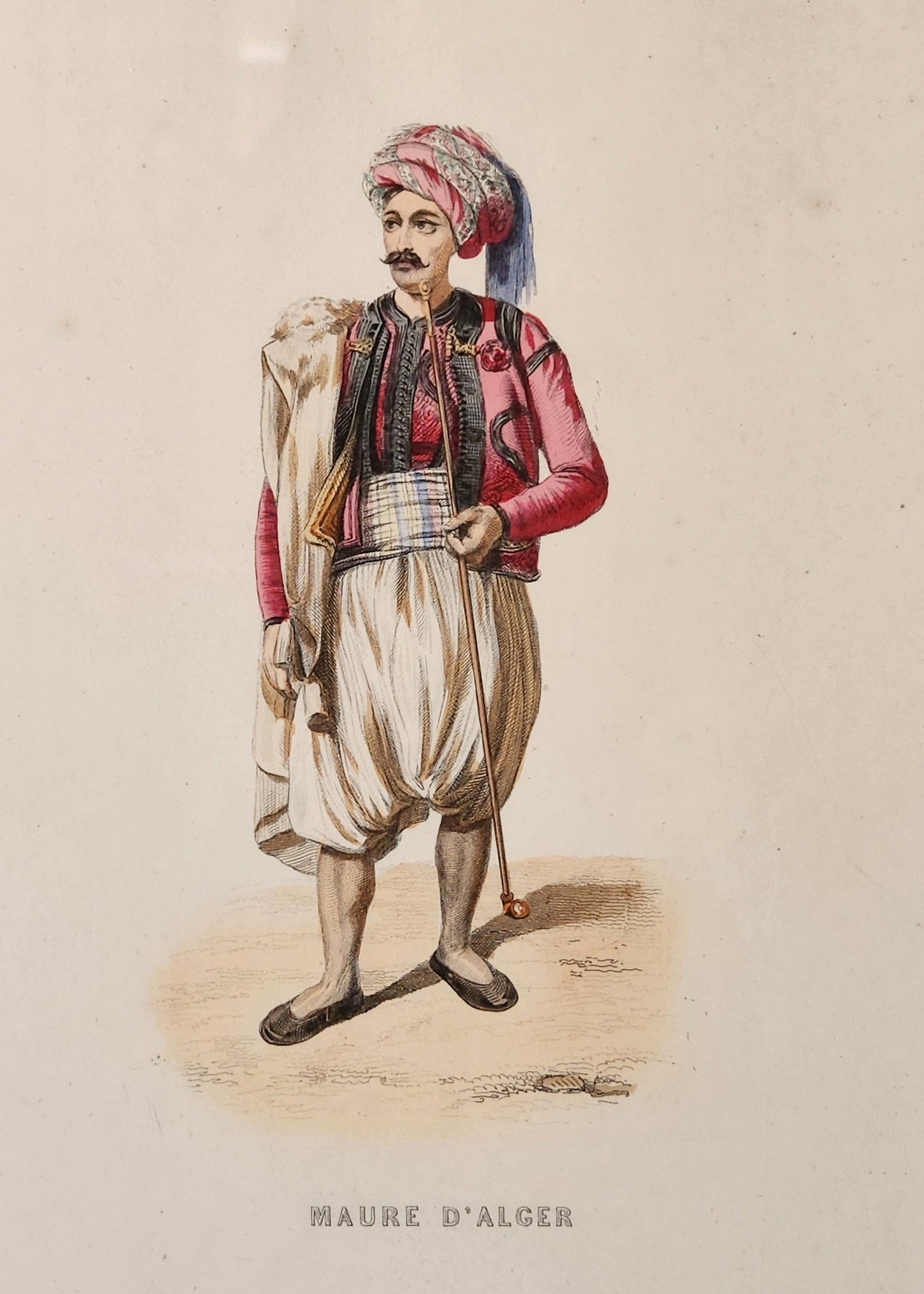 Traditional Algerian attire with a turban and colorful clothing on a plain background.